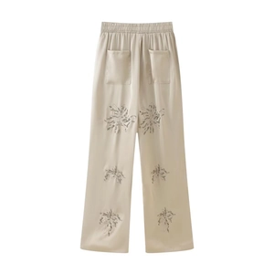 Detail of champagne satin wide-leg trousers with elastic waist and delicate floral prints