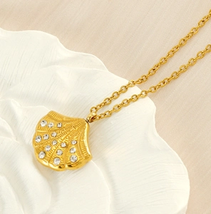 Detail of 18K gold shell pendant with sparkling crystals on white floral base