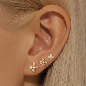 Detailed view of three gold flower stud earrings with sparkling crystals on ear