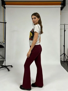 Vista laterale di t-shirt bianca con stampa e pantaloni a zampa bordeaux su modella