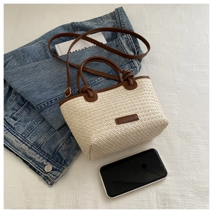 Detail of hand-woven straw tote with brown leather trim and adjustable shoulder strap