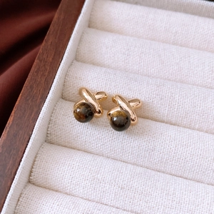 Macro shot of gold-plated X-shape stud earrings with center brown tiger eye stone bead
