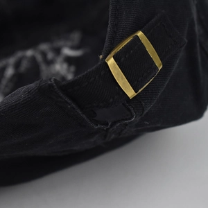 Close-up of matte gold metal buckle and adjustable cotton strap on black beret hat