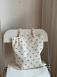 Detail of grey floral tote bag with black dots and bow pattern on a white chair