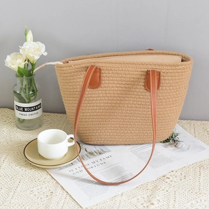 Detail of hand-woven straw tote with brown leather handles and white stitching