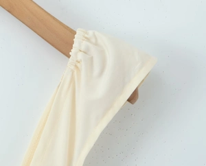Detailed close-up of the beige off-shoulder dress fabric and pleated shoulder strap texture