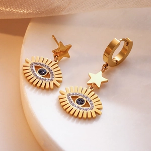 Gold asymmetric star and evil eye drop earrings set with white crystals on a white tray