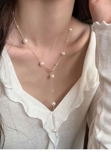 Detail of Y-shaped gold pearl necklace with various sized pearls on a white blouse