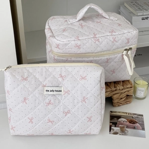 Detail of white quilted makeup bags with pink bow pattern and golden zippers