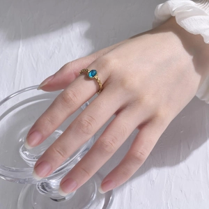 Close-up of twisted gold steel ring featuring a vibrant oval blue zircon on model's finger