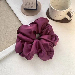 Close-up of oversized dark purple satin scrunchie with elegant silk-like pleated texture