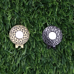 Detailed view of silver and bronze golf ball markers with hat clips on green turf background