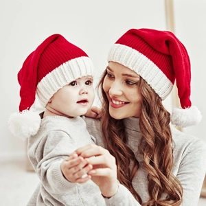 Close-up of mother and baby wearing red and white knitted Christmas hats with fur pom-poms