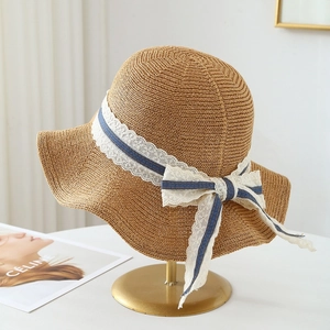 Detail of wide brim straw sun hat featuring a striped blue and white lace ribbon bow
