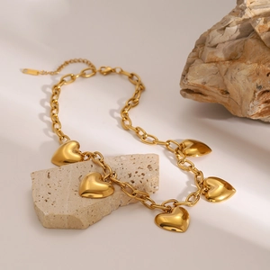 Polished gold heart charm necklace with chunky oval links on natural stone background