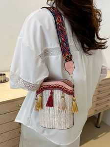 Close-up of woven bucket bag with pink trim, colorful geometric strap and tassels