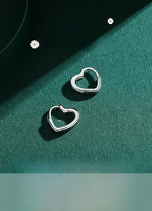 Gros plan de créoles en forme de cœur en argent fin S925 poli sur fond vert de luxe