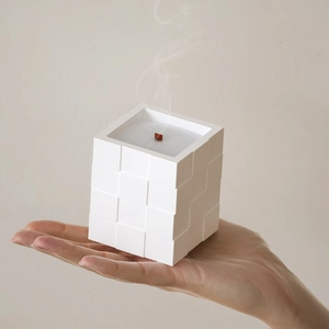 Macro shot of white cube candle with grid texture and burning wooden wick in hand