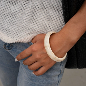 Dettaglio del bracciale in resina marmorizzata crema con maglione bianco e jeans