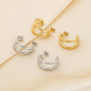 Detail of double-layer C-shape earrings in gold and silver on beige silk fabric