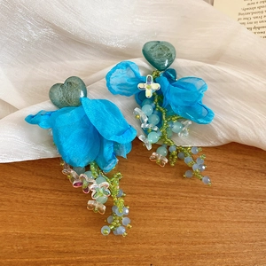 Detailed close-up of blue fabric flower earrings with green resin hearts and bead tassels