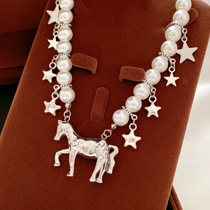 Detailed view of silver horse pendant and star charms on a white pearl necklace