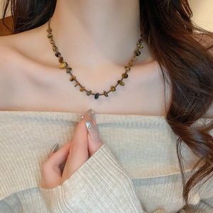 Gros plan détaillé du collier en perles d'oeil de tigre sur un pull beige