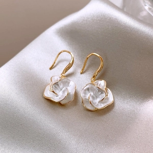 Macro shot of gold-plated white camellia flower drop earrings on soft silk fabric