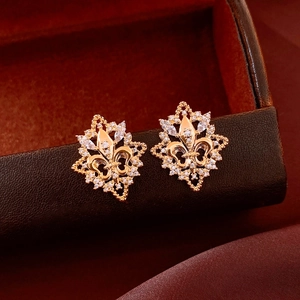Macro view of gold fleur-de-lis earrings with cubic zirconia on a luxury leather box