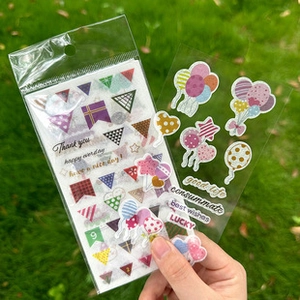 Transparent PET decorative stickers with balloons and banners held over a grass background