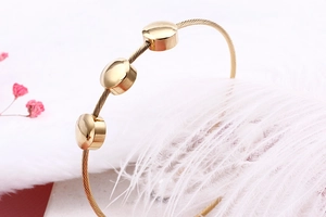 Macro shot of gold twisted cable bangle featuring three polished round beads on white feathers
