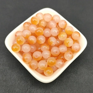 Detailed view of 8mm orange and translucent white gradient glass beads in a white dish
