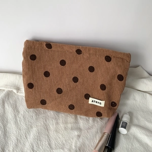Detailed texture of khaki corduroy makeup bag with brown polka dots and woven label