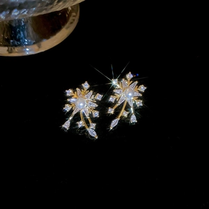 Macro view of snowflake earrings with crystal zircons and a pearl center on dark background