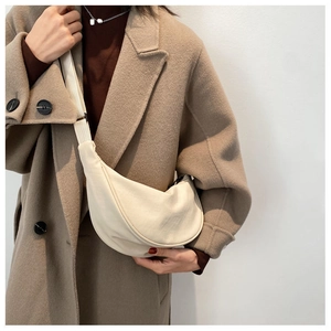 Close-up of a minimalist cream-colored crescent bag with an adjustable wide strap