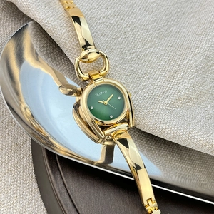 Macro shot of gold horseshoe case watch with green dial and polished metal bracelet