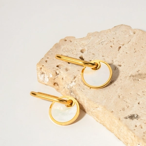 Macro shot of gold plated earrings featuring white mother of pearl on a beige stone