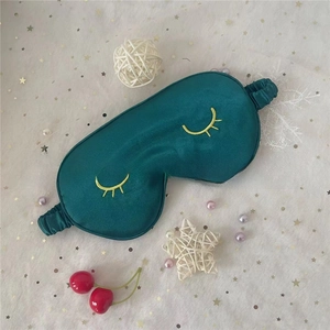 Close-up of dark green silk sleep mask featuring yellow eyelash embroidery on mesh