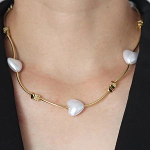 Golden tubular link necklace featuring three white heart-shaped pearls on a female model