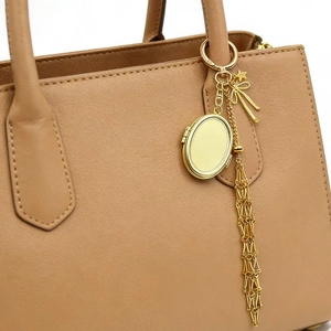 Dettaglio del ciondolo a cornice ovale in metallo dorato con nappa su borsa color cammello