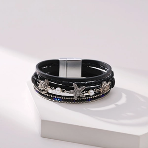 Detail of multi-layer leather bracelet with silver starfish and turtle charms on a white stand