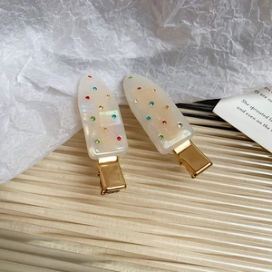 Detailed macro of pearl white acrylic hair clips with multi-colored crystals and gold metal