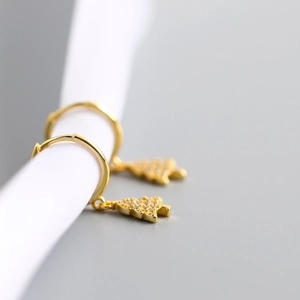 Close-up of golden Christmas tree hoop earring with zircon stones on white ribbon
