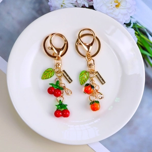 Close-up of fruit keychains featuring persimmon and cherry charms with gold hardware