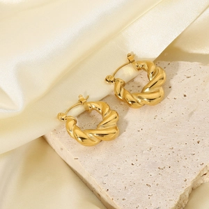 Macro shot of gold plated stainless steel twisted hoop earrings on stone and silk