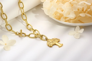 Detailed close-up of a gold-toned chunky chain necklace with a heart-leaf tree pendant