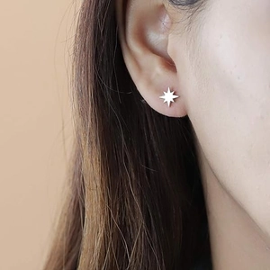 Minimalist silver eight-pointed star stud earrings worn by a model in a close-up side view