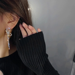 Close-up of sparkling bow tassel earrings with white rhinestones on a female model