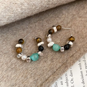 Macro detail of Tiger Eye and pearl beaded C-shaped earrings on a warm fabric background