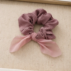 Detailed view of pink plaid fabric scrunchie with a matching chiffon bow on linen